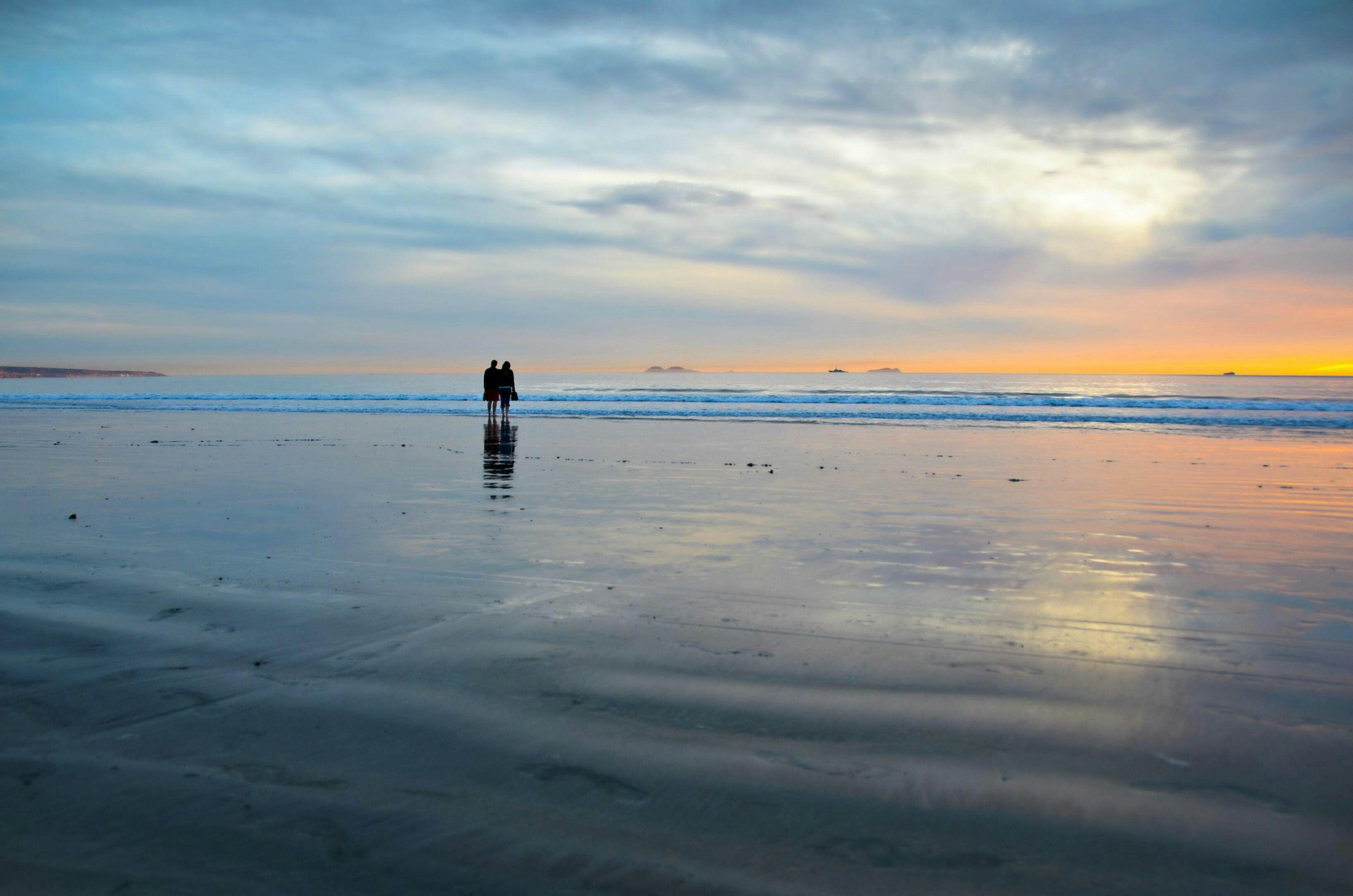 2E5BKXB Young couple silhouettes on the Silver Strand Beach wet sand  watching the sunset at Coronado Island, San Diego Southern California USA.
